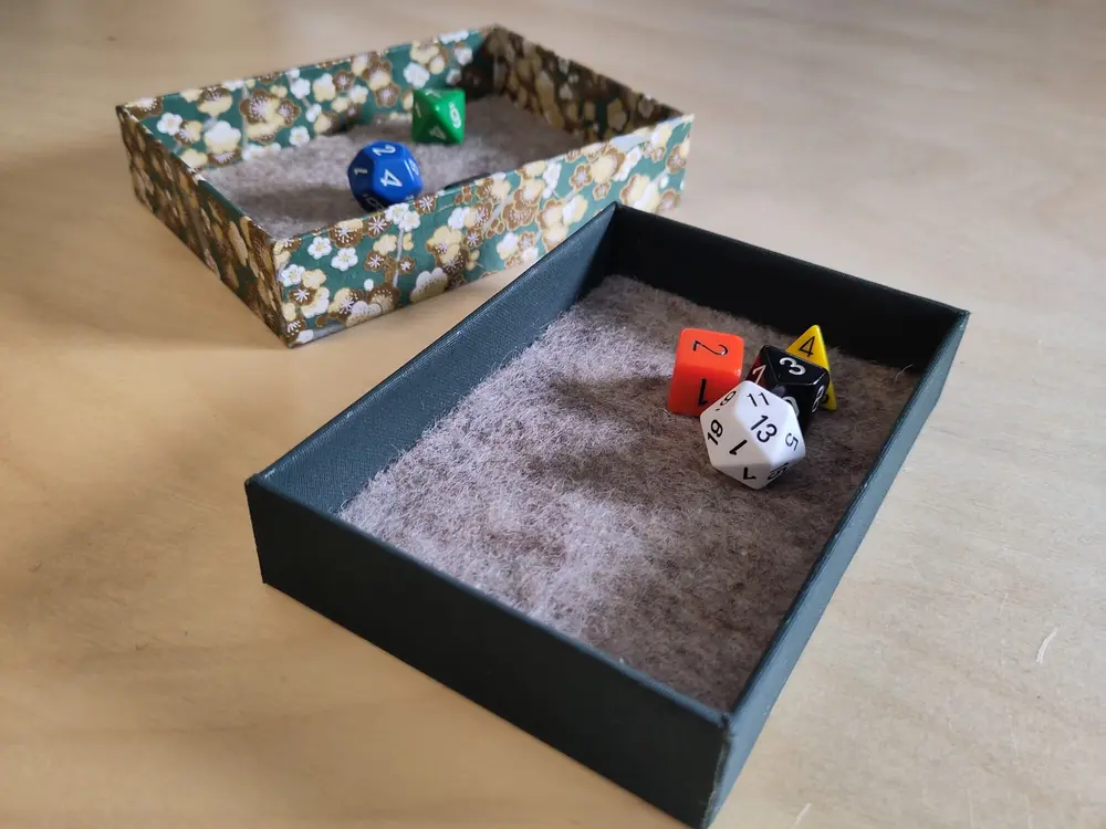 Image of dice box with some dice in both the box and the lid. Both the box and the lid are padded with felt.